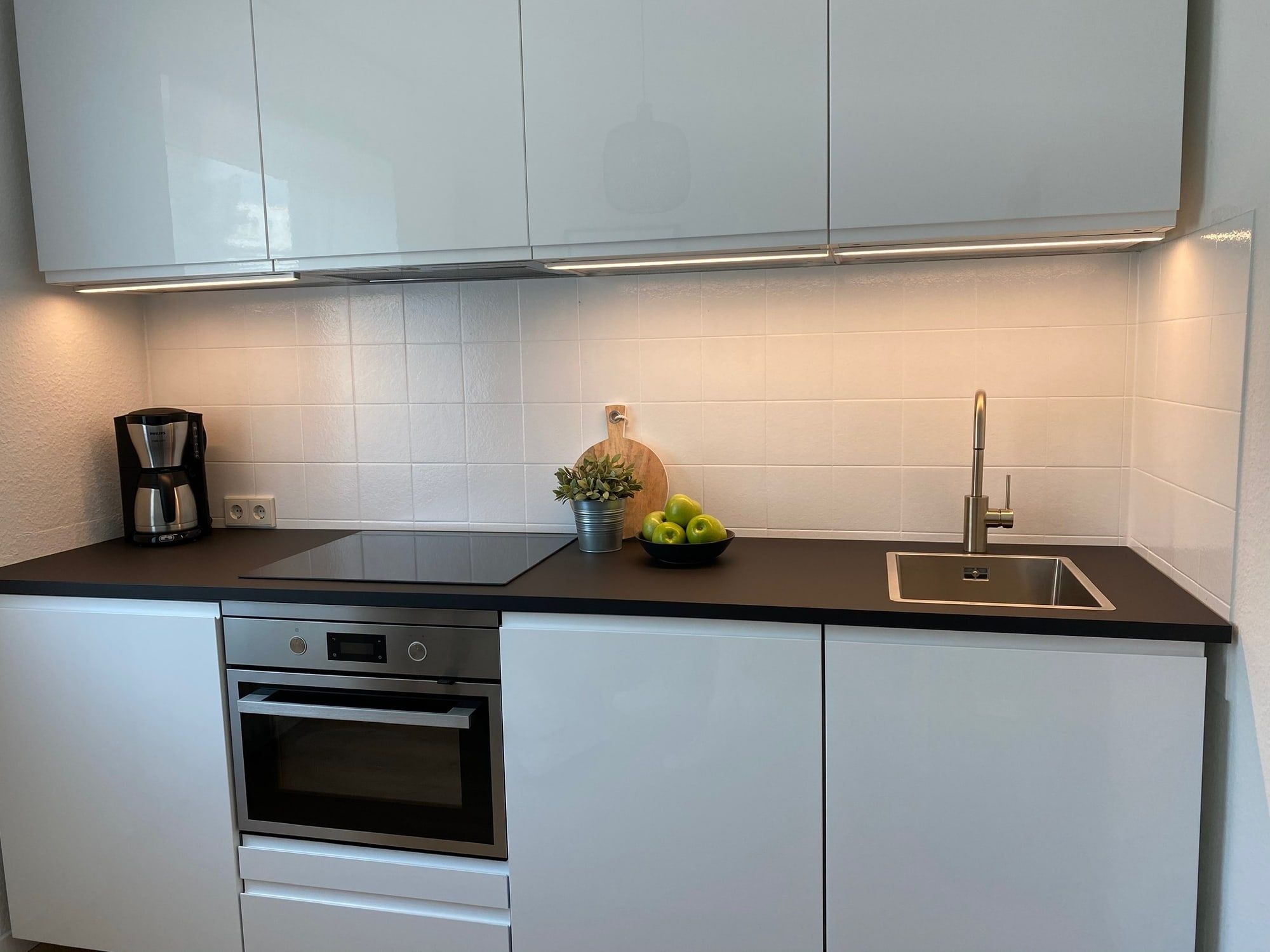 A modern kitchen with white cabinets, stove, sink, and coffee maker.