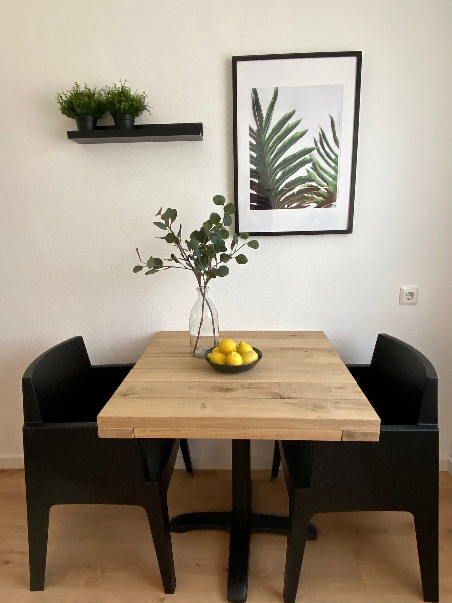 Moderner Esstisch mit zwei schwarzen Stühlen, einer Vase mit Zweigen und einer Schale mit Zitronen.