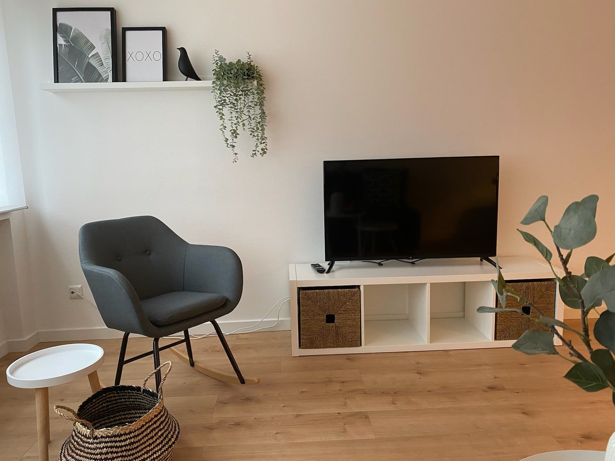 Gemütliches Wohnzimmer mit grauem Sessel, Fernseher und Dekoration.