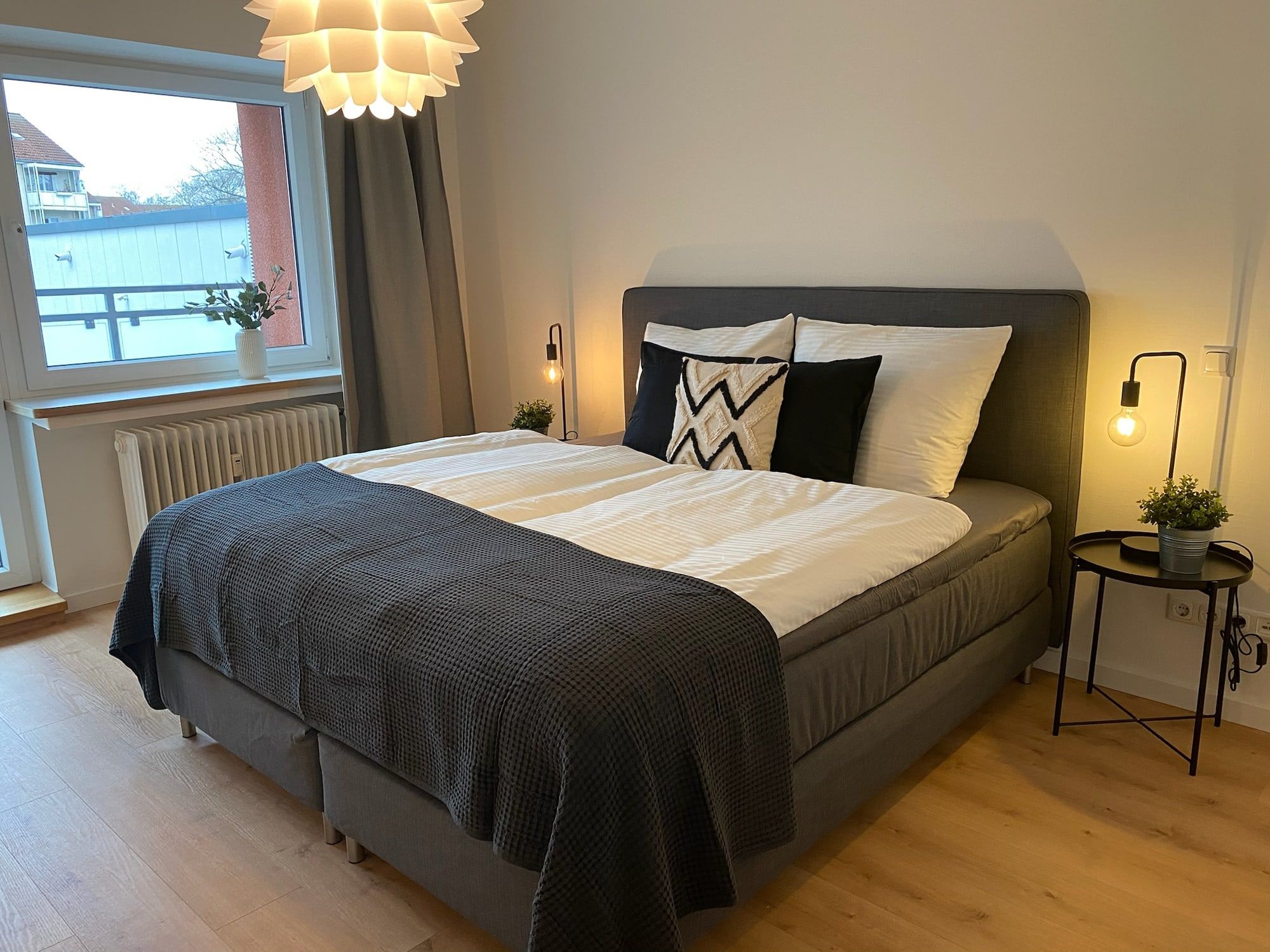 Helles Schlafzimmer mit großem Fenster, Doppelbett und moderner Beleuchtung.