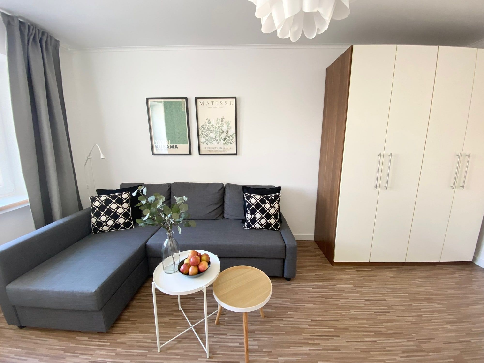Helles Wohnzimmer mit grauem Ecksofa, zwei Tischen und großem Kleiderschrank