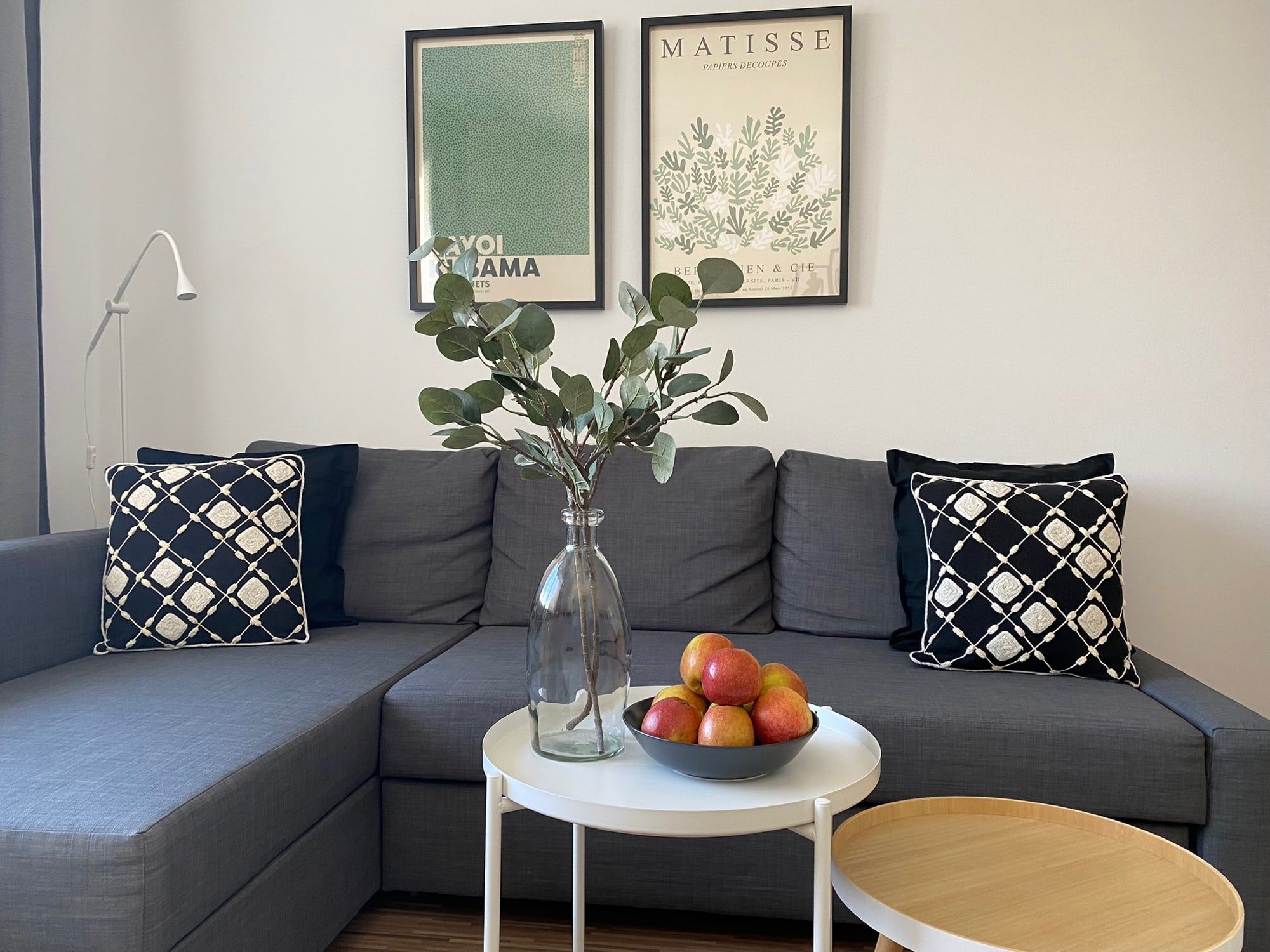 Ein graues Sofa mit schwarzen Kissen und einem weißen Tisch mit Obstschale und Vase davor.