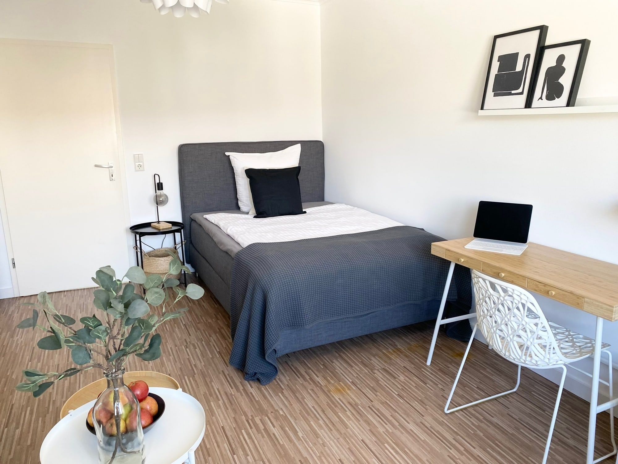 Helles Einzelzimmer mit grauem Bett und Schreibtisch