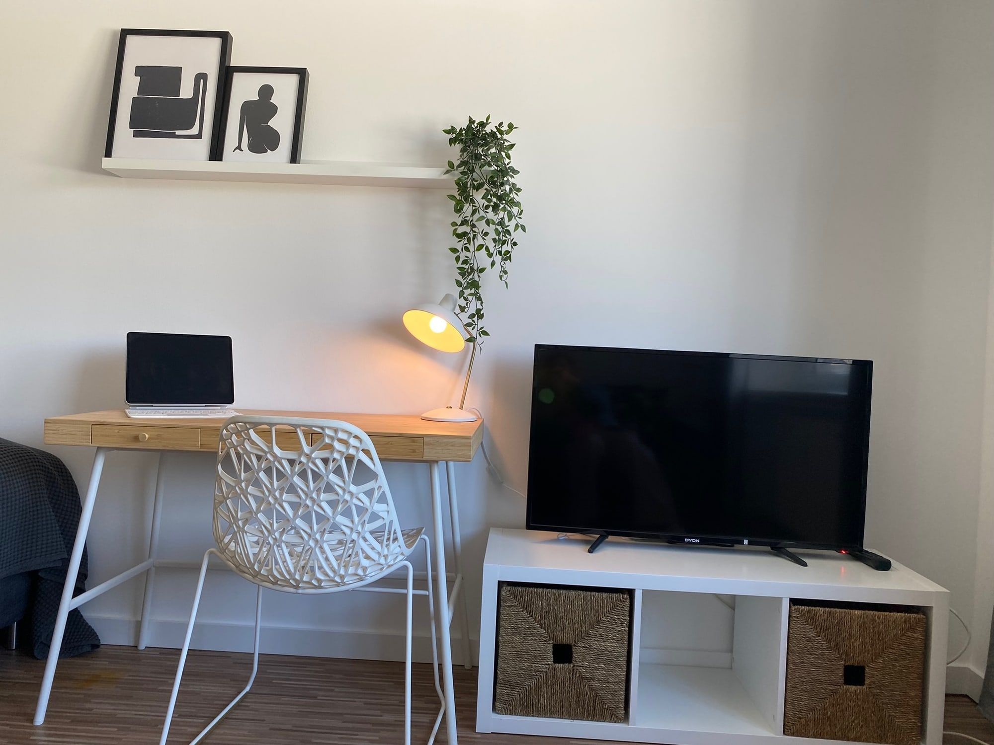 Un espace de travail lumineux avec bureau, chaise, lampe, télévision et deux cadres au mur.