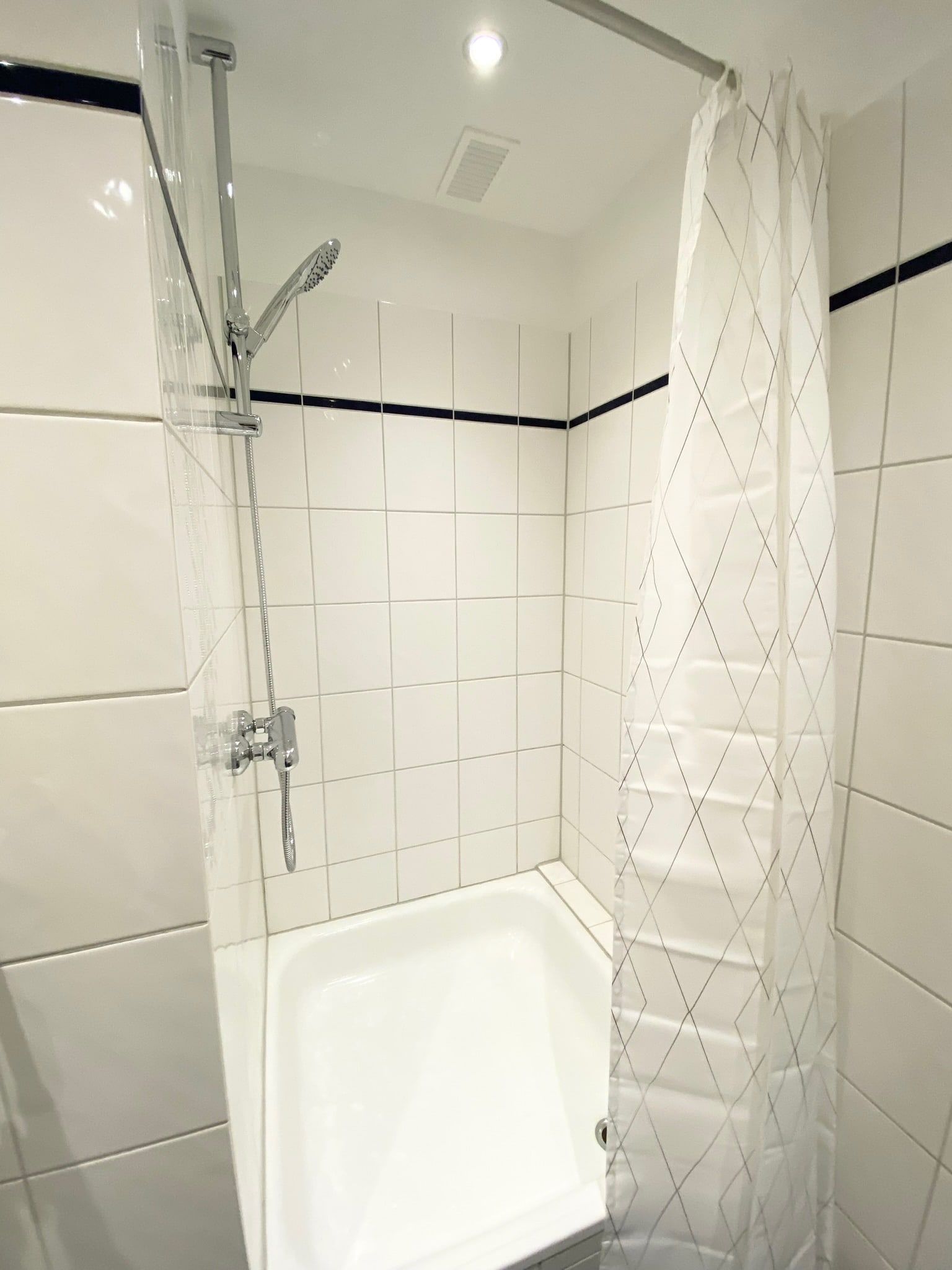 Weiße Dusche mit Duschvorhang und verchromtem Duschkopf
