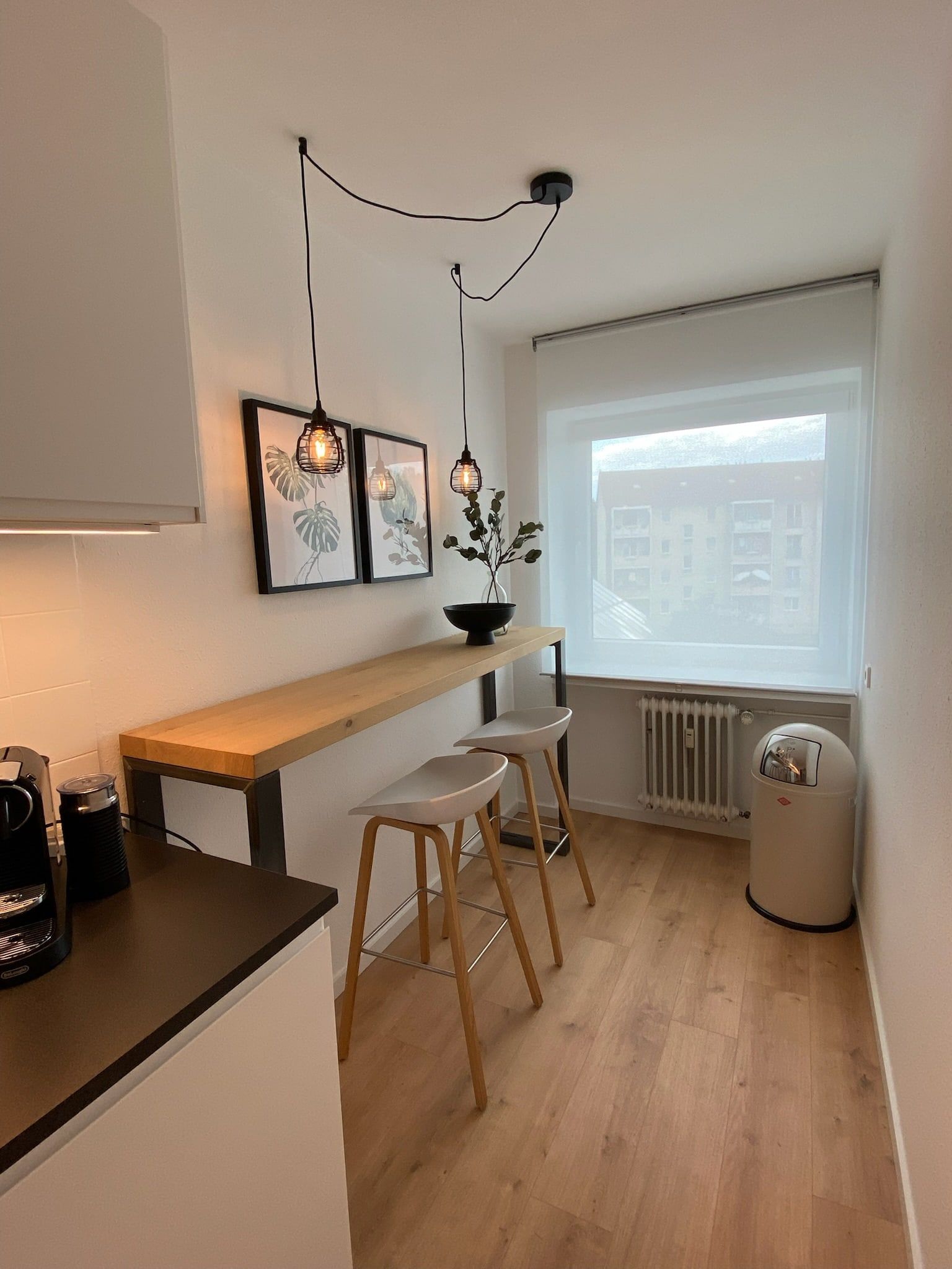 Kleine Küche mit Holzbar, zwei Barhockern und zwei hängenden Lampen an der Wand.