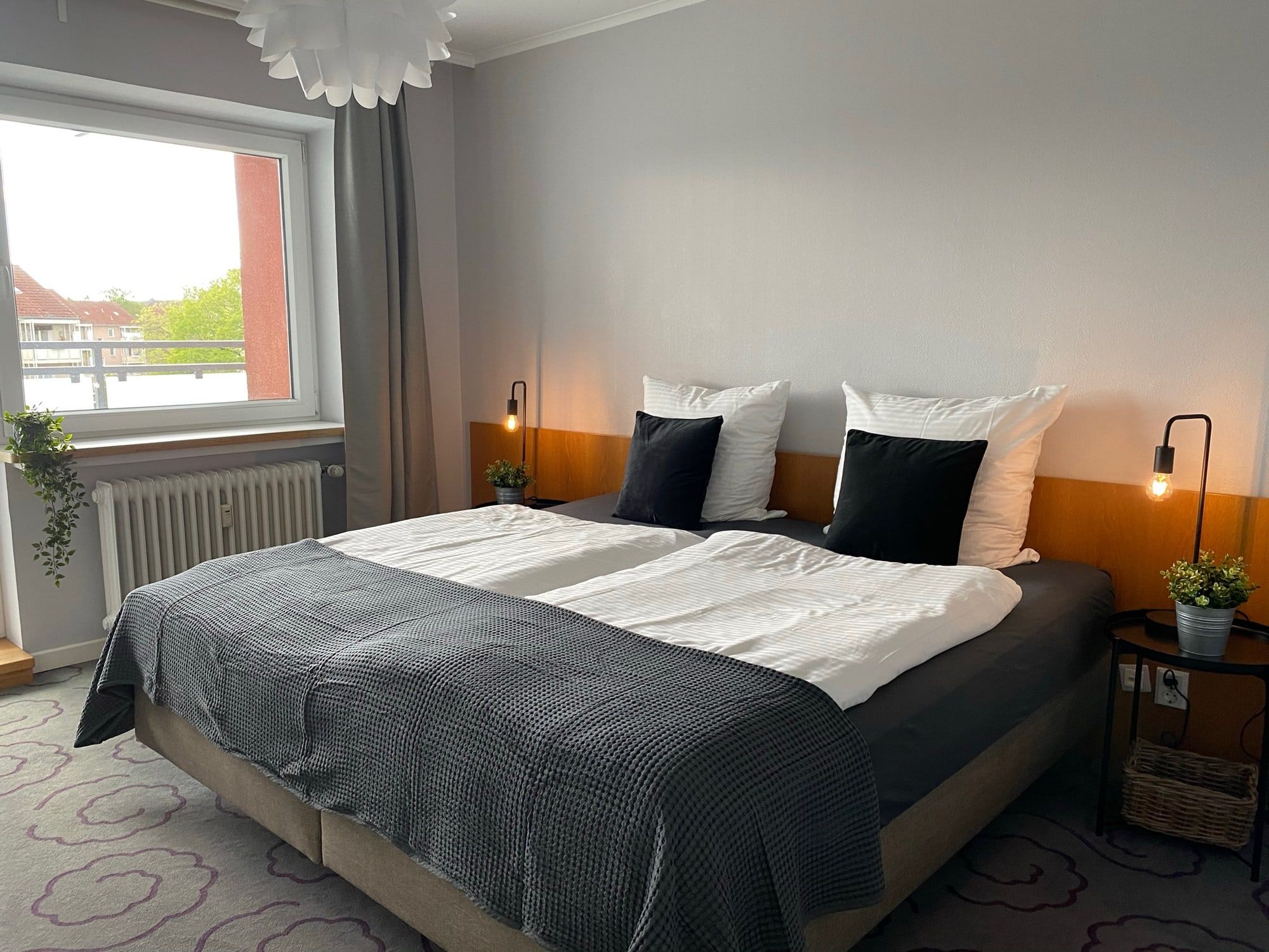 Hell eingerichtetes Schlafzimmer mit großem Fenster und Doppelbett.