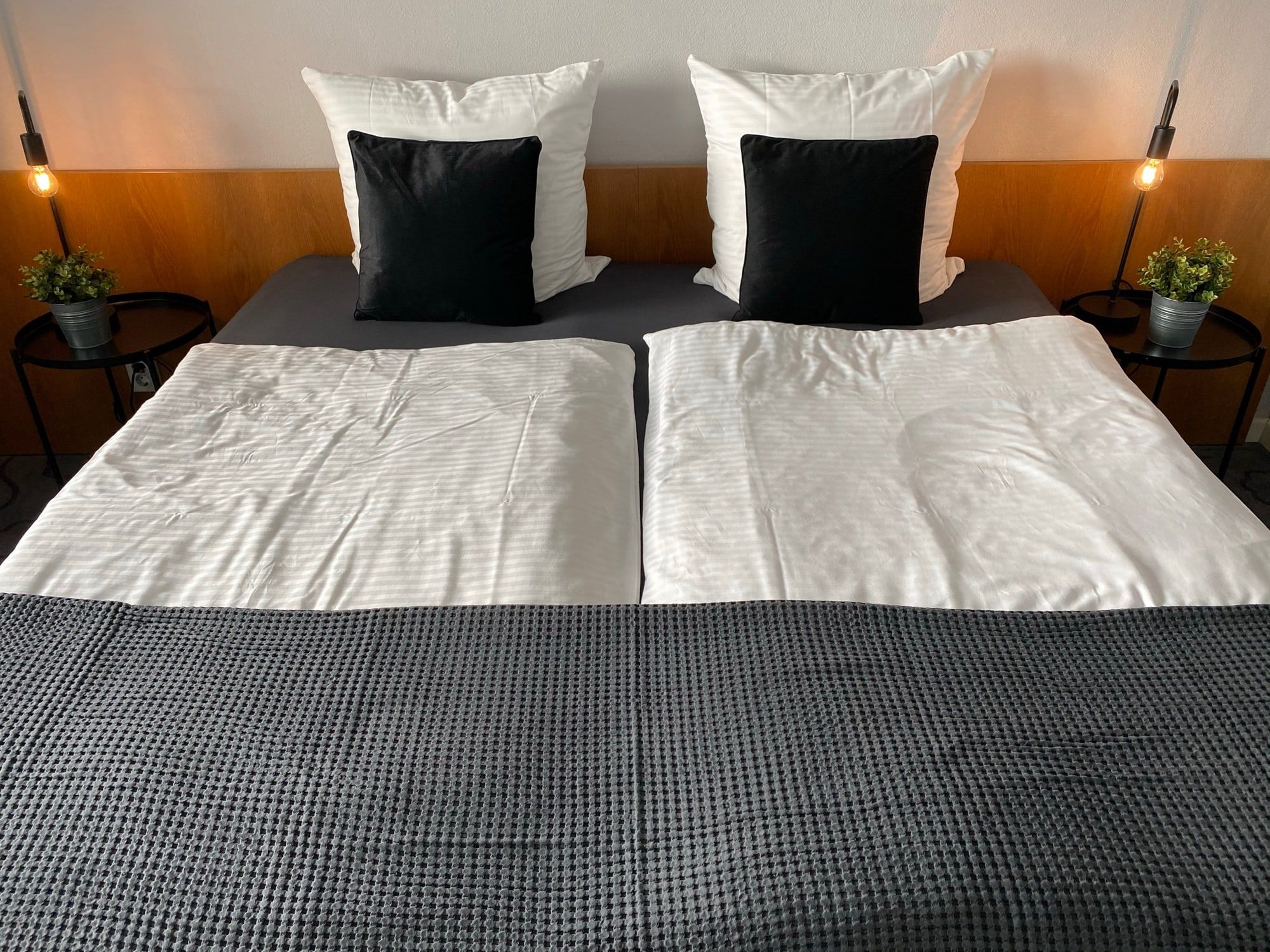 Ein ordentlich gemachtes Doppelbett mit weißen und schwarzen Kissen sowie grauer Decke.