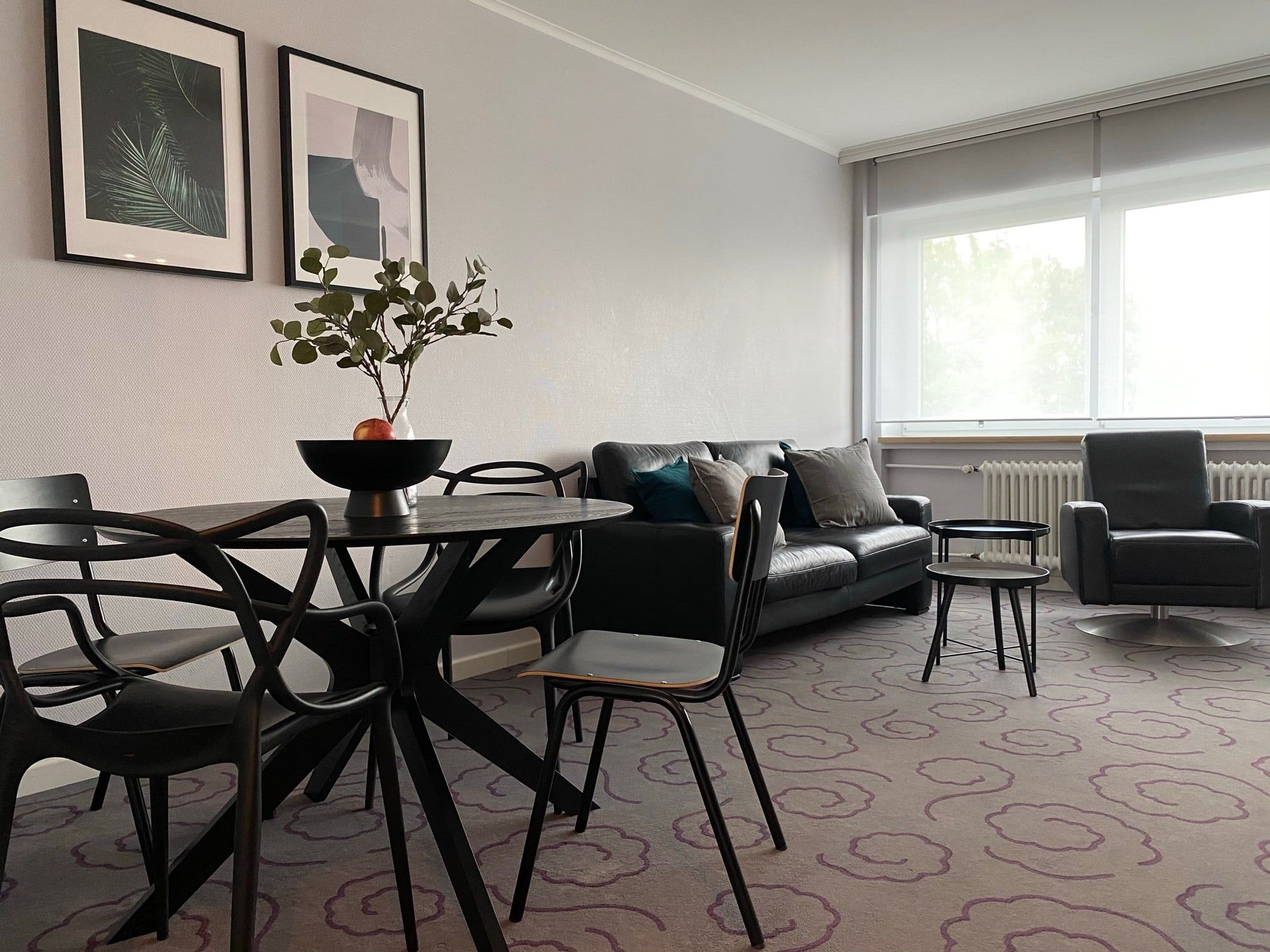 Helles Wohnzimmer mit schwarzem Sofa, Sessel und Esstisch mit Stühlen