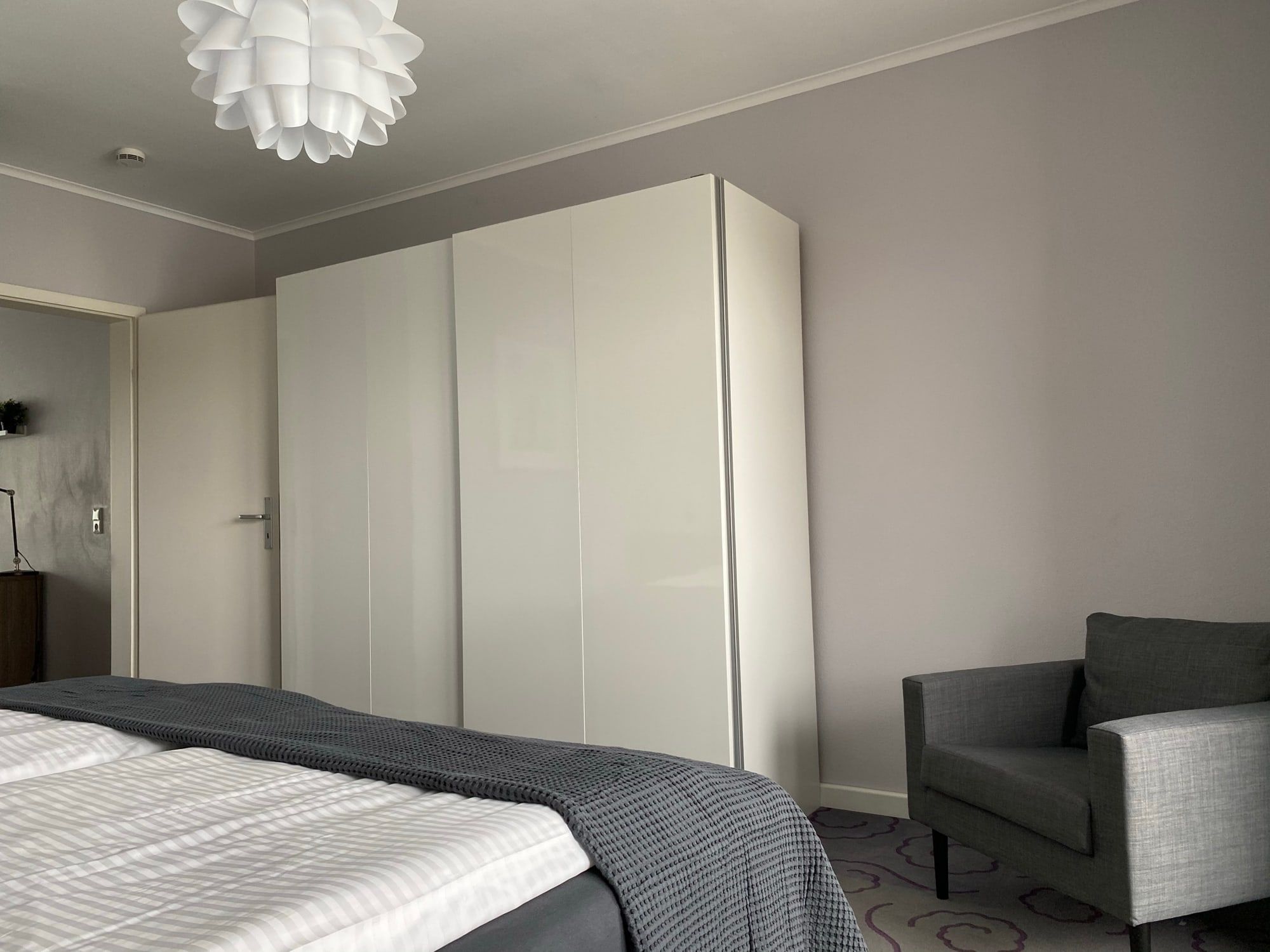 Ein schlicht eingerichtetes Schlafzimmer mit grauem Sessel und weißem Kleiderschrank.