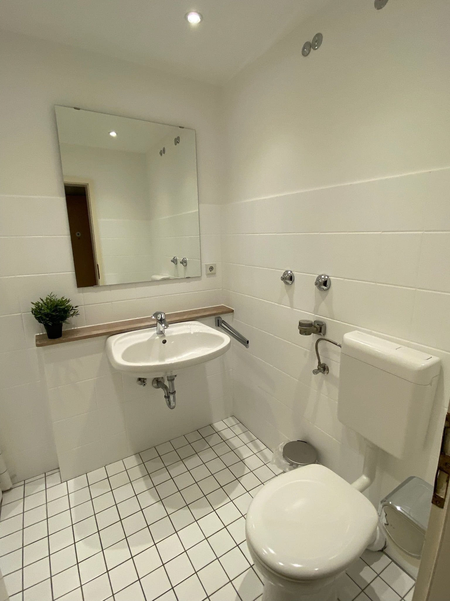 Ein kleines Badezimmer mit weißem Waschbecken, Toilette und großem Spiegel.