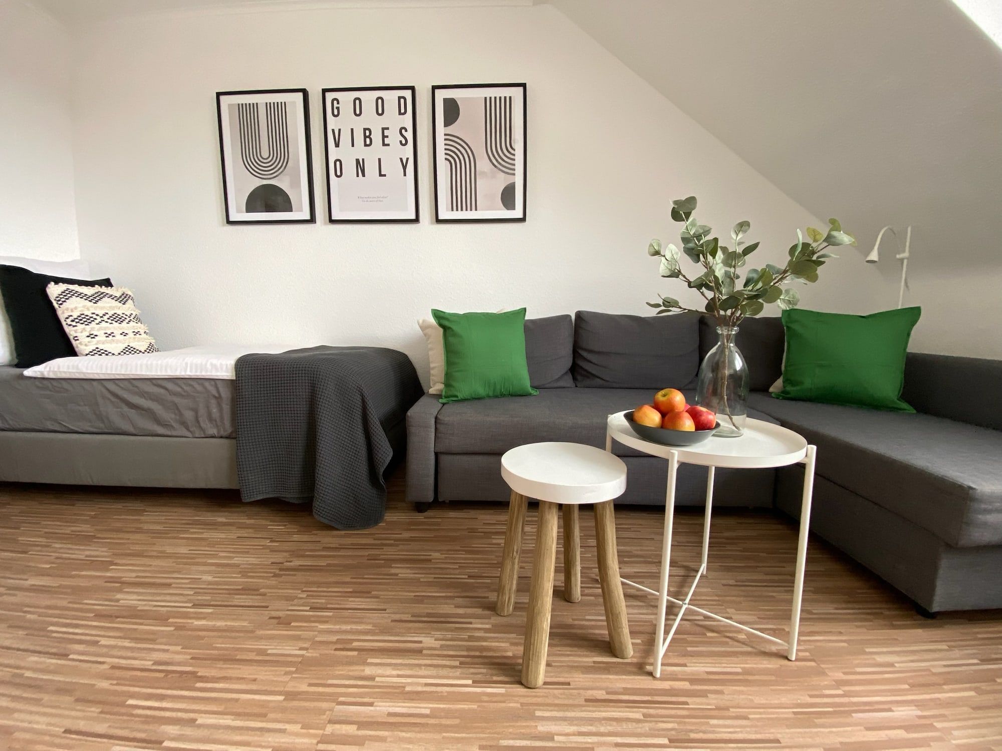 Ein modernes Wohnzimmer mit grauem Ecksofa, grünem Kissen und dekorativen Bildern an der Wand.
