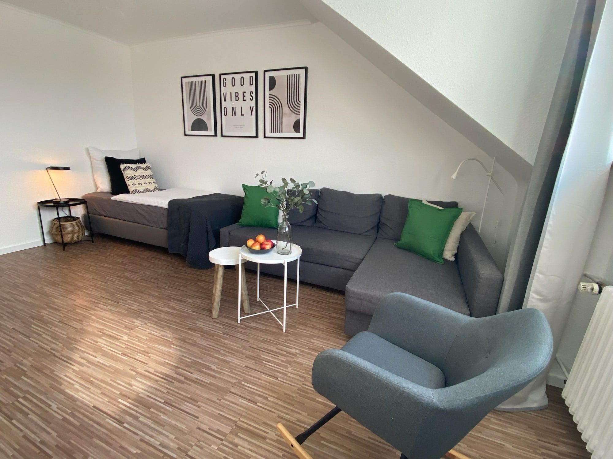 Helles Wohnzimmer mit grauem Ecksofa, Einzelbett und moderner Dekoration.